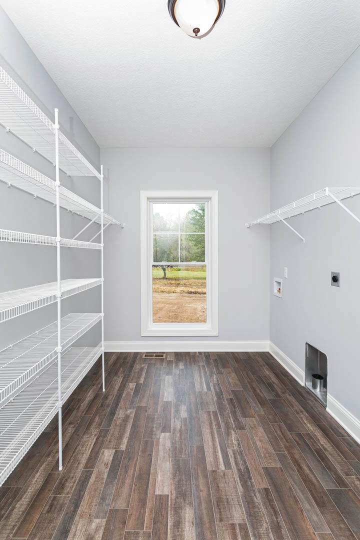 White built-in shelves along plaster walls, large window overlooking grassy field, hardwood floor, exposed light bulb fixture
