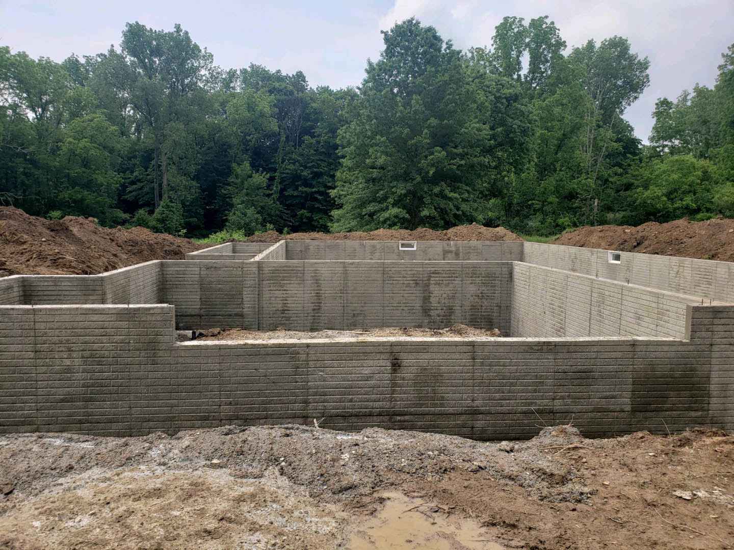 Concrete foundation slab surrounded by dirt, trees, and woodland background