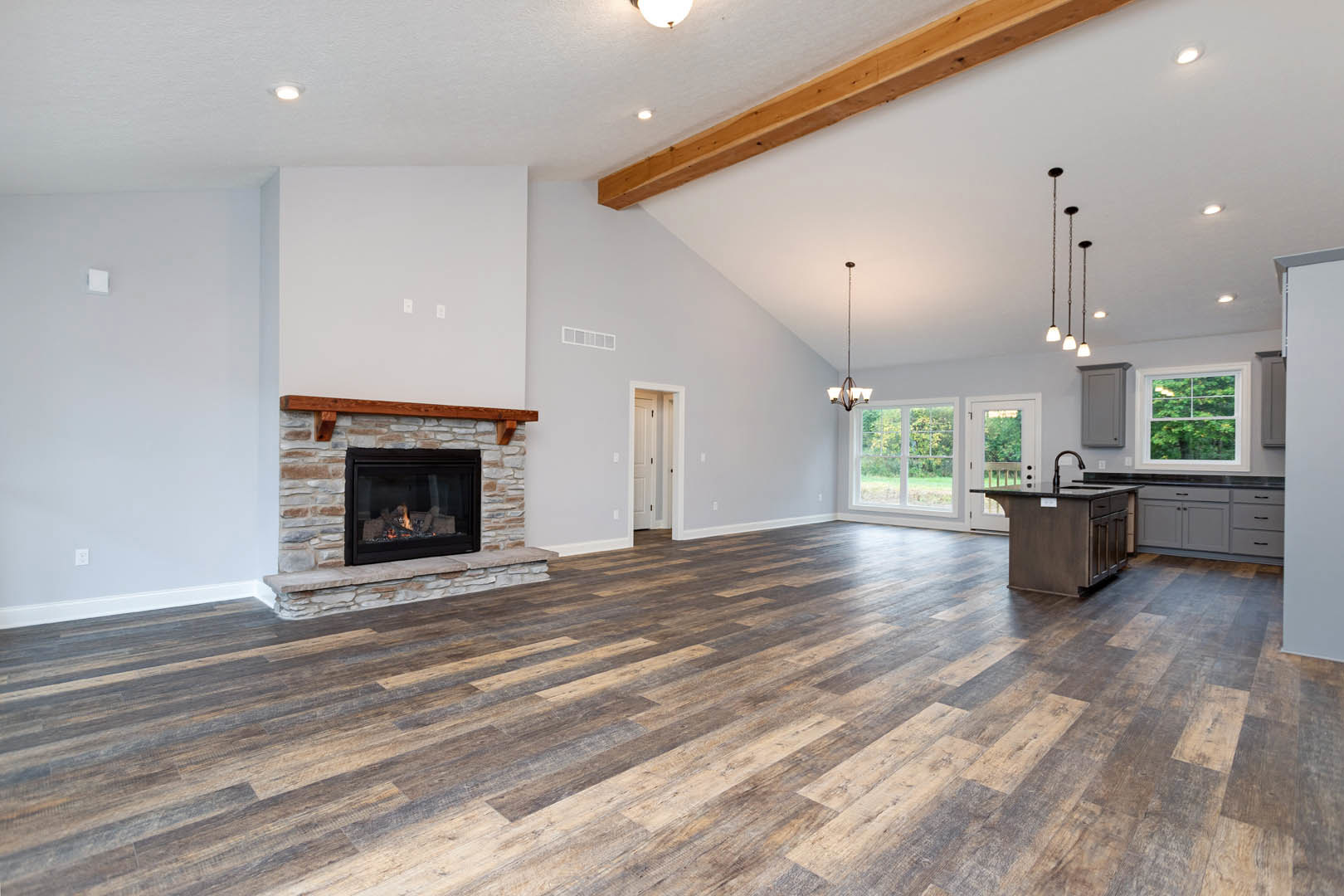 Spacious living room featuring hardwood floors, active fireplace with burning logs, white door with black knobs, large window overlooking trees