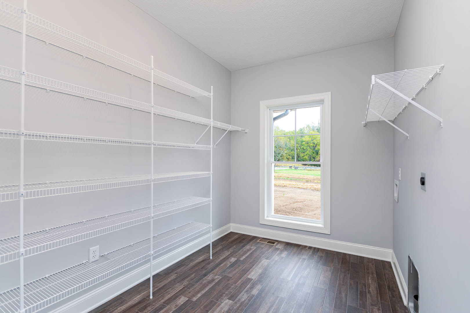 White built-in shelves against a plaster wall, wood floor with white trim, large window overlooking field and trees.