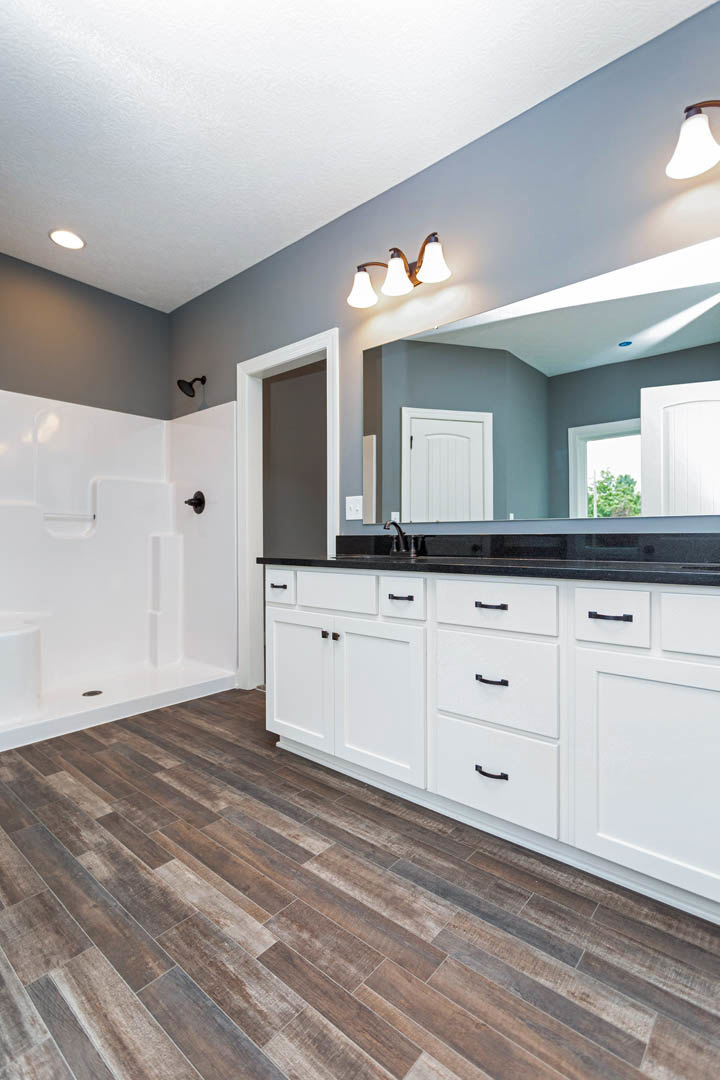 Bathroom with white cabinets, freestanding bathtub, wood flooring, blue accent wall, three-light fixture, and white door