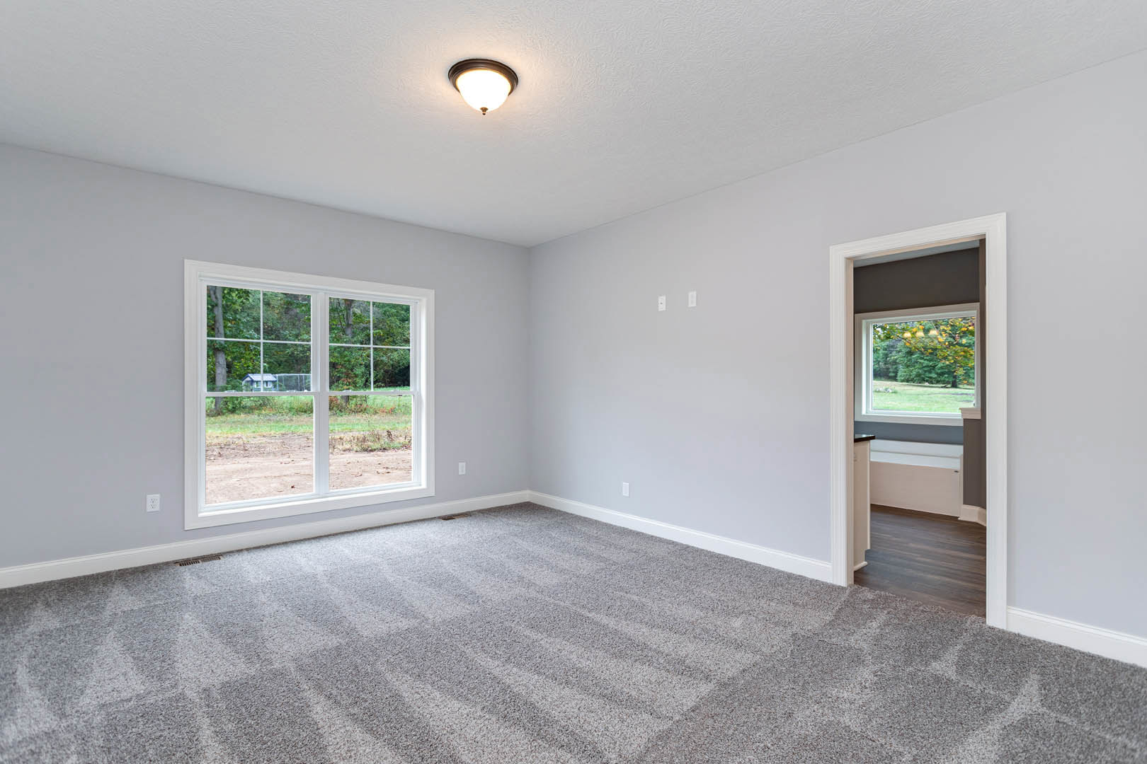 Carpeted room with large window overlooking green yard, white walls, and ceiling light fixture