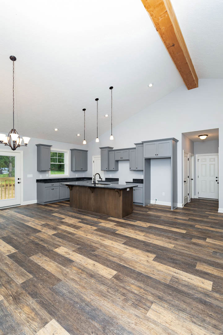 Spacious kitchen featuring wood flooring, black granite countertops, white cabinetry with black knobs, wooden ceiling beam, and a white door adjacent to a dining table.