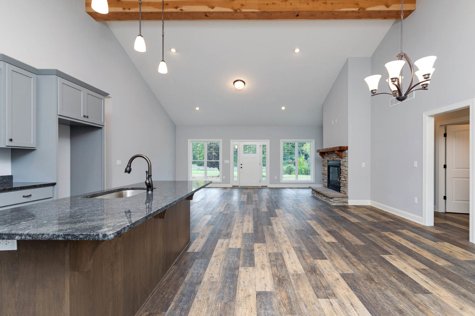 Open-concept kitchen and living room with wood flooring, white cabinetry, stone countertops, stainless steel sink, glass-paneled door, large windows overlooking trees, and a modern