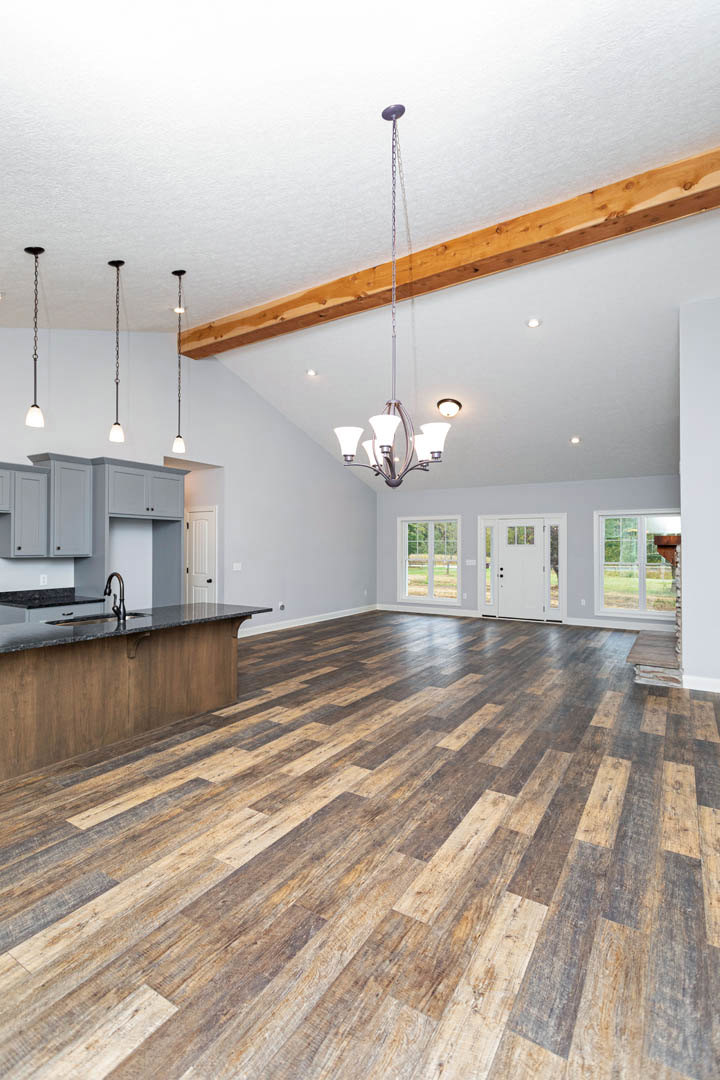 Spacious open-concept kitchen and living area featuring wood flooring, central kitchen island with sink, white door with glass panes, modern five-light ceiling fixture, and sleek