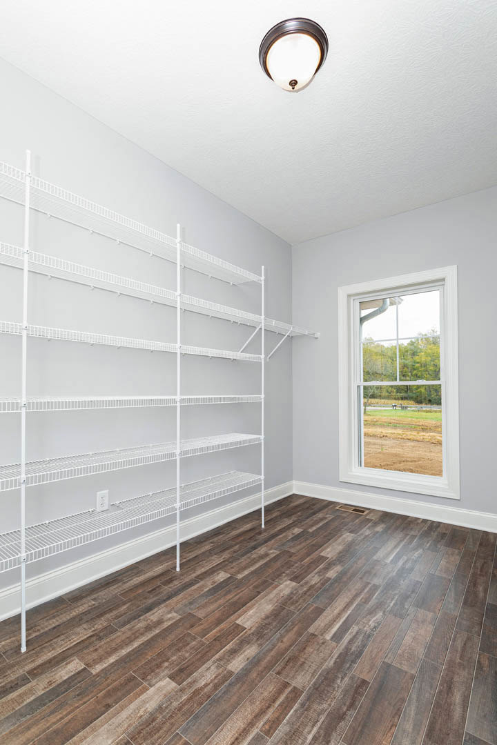 Empty room with built-in white shelves, wood flooring, ceiling light fixture, and window overlooking field and trees