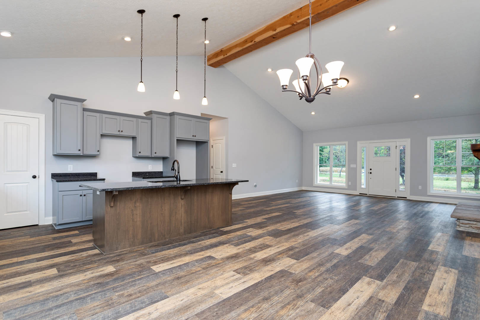 Open kitchen and dining area with light wood flooring, white cabinetry, stone countertop with built-in sink, modern chandelier, and large window overlooking outdoor greenery.