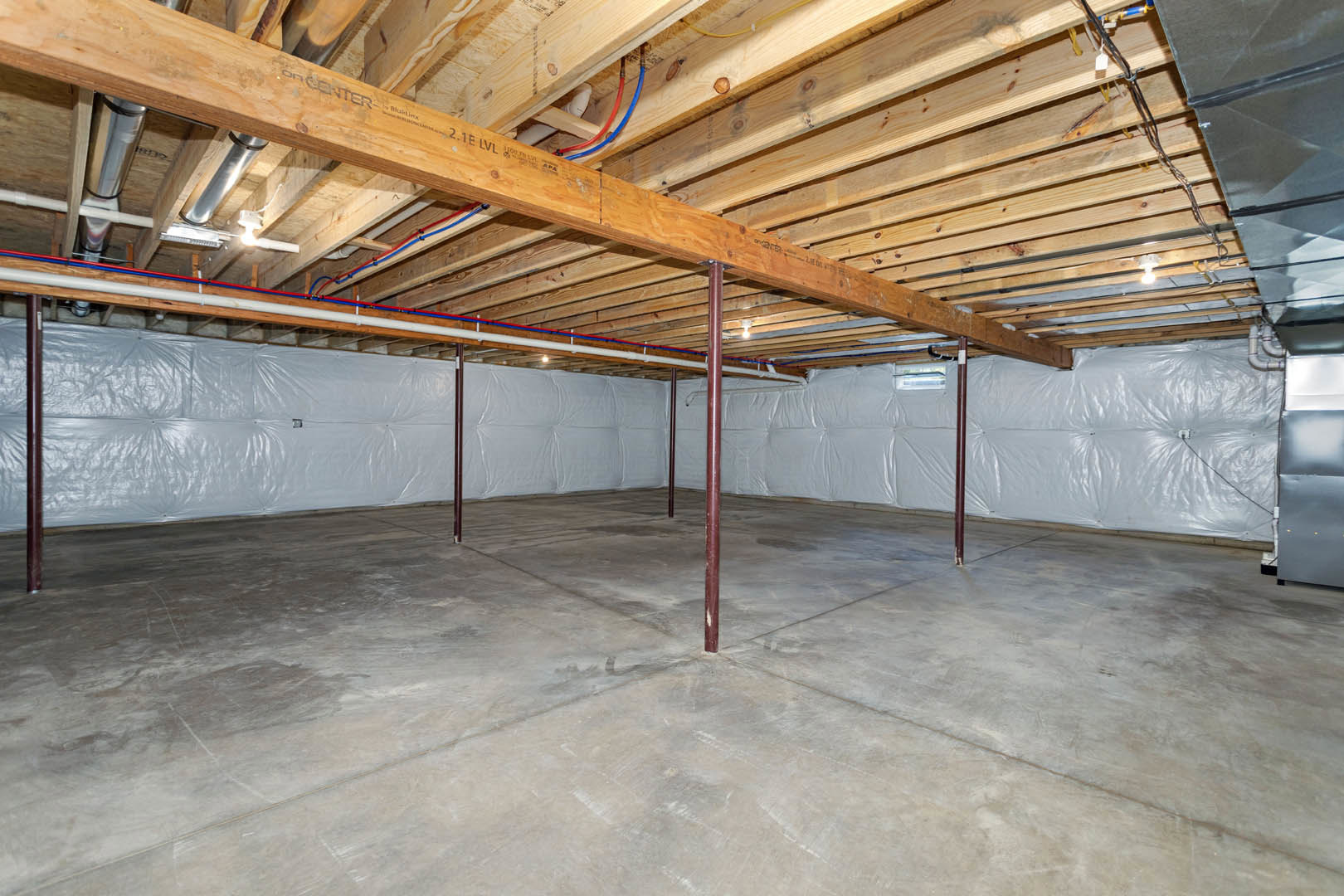 Exposed wooden beams and wood plank ceiling above concrete floor with steel support pole in unfinished basement room