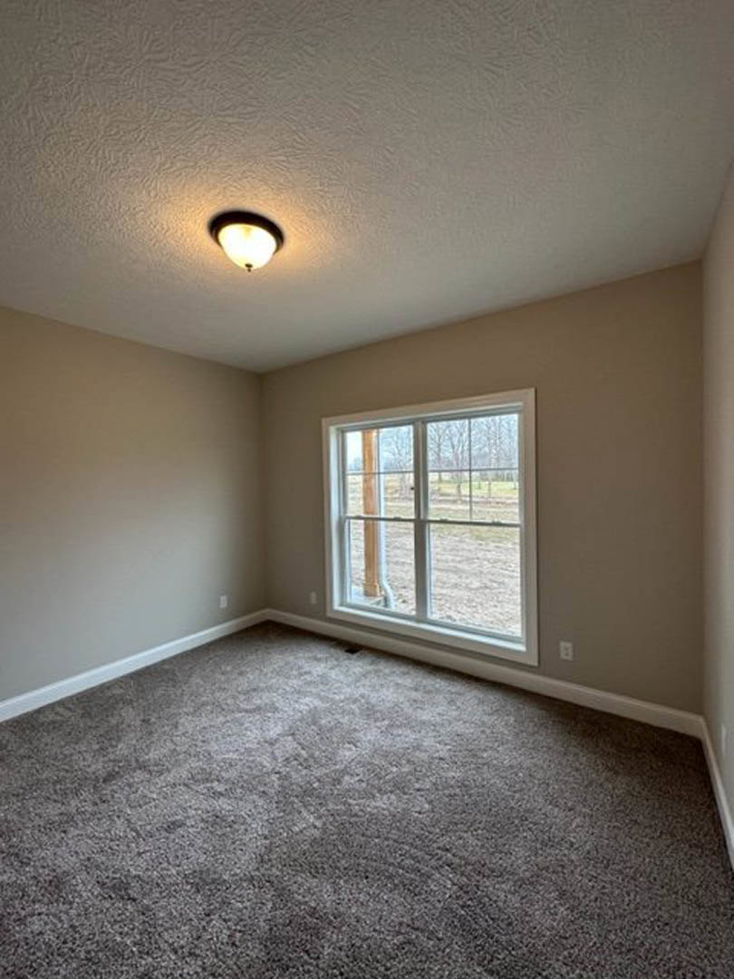 Bright room with white walls, large window overlooking grassy field, soft grey carpet flooring, recessed ceiling light fixture