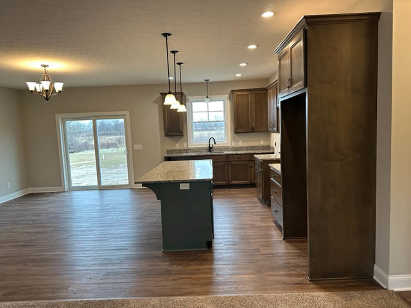 Spacious kitchen featuring a large central island with light stone countertop, wood flooring, white cabinetry, stainless steel sink, four-shade pendant light fixture, and a window
