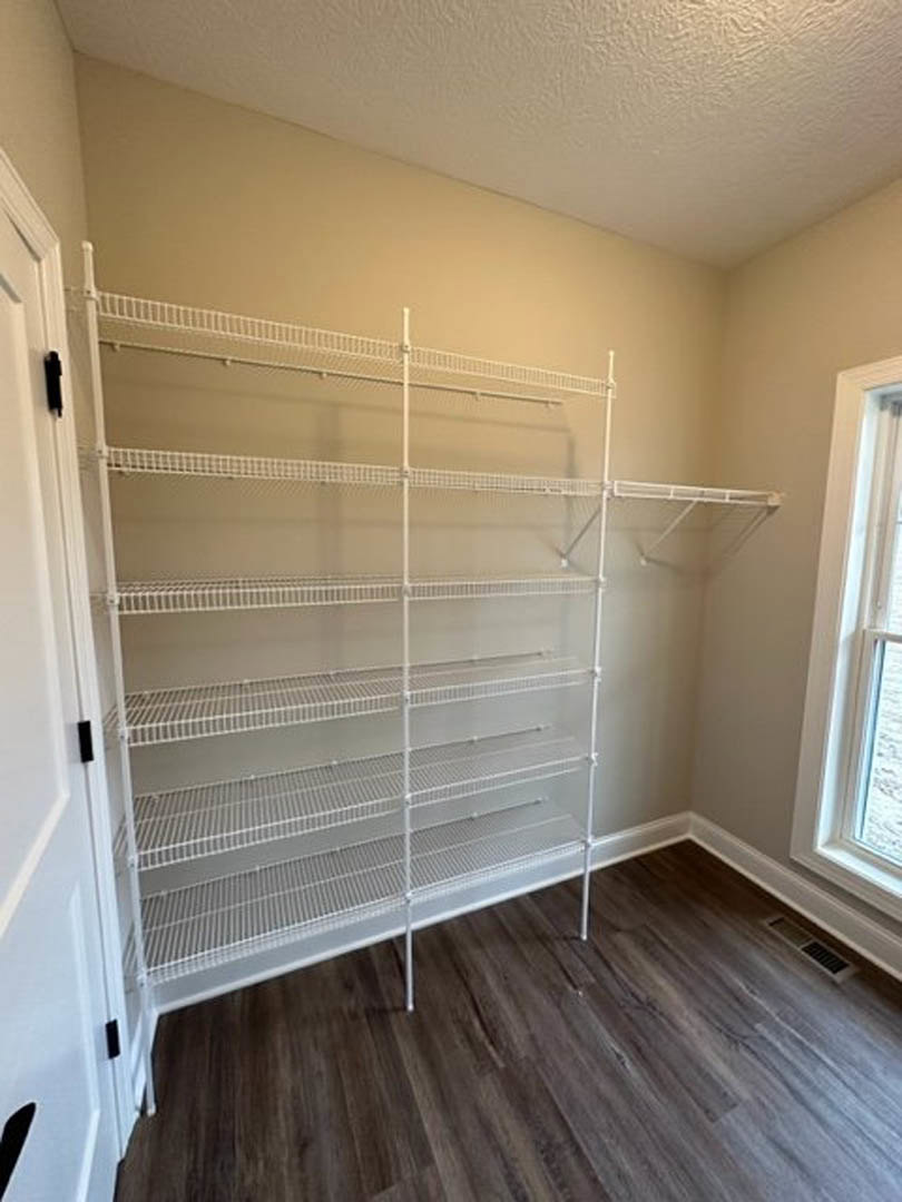Empty closet with built-in white shelves, wood flooring, window, and wall vent
