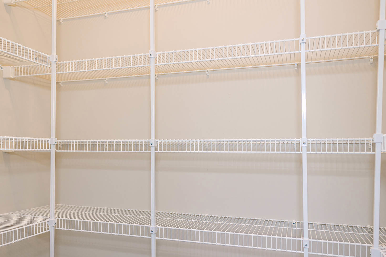 White wire shelving unit with wheels positioned against a white wall in a room, adjacent to a ladder.