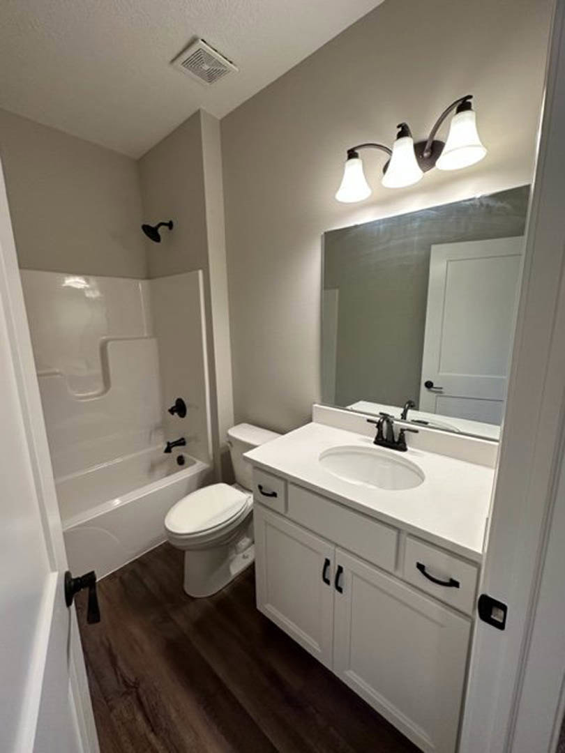 Modern bathroom featuring a white toilet and rectangular sink with black faucet, wall-mounted mirror, light gray tile walls, and minimalist fixtures.