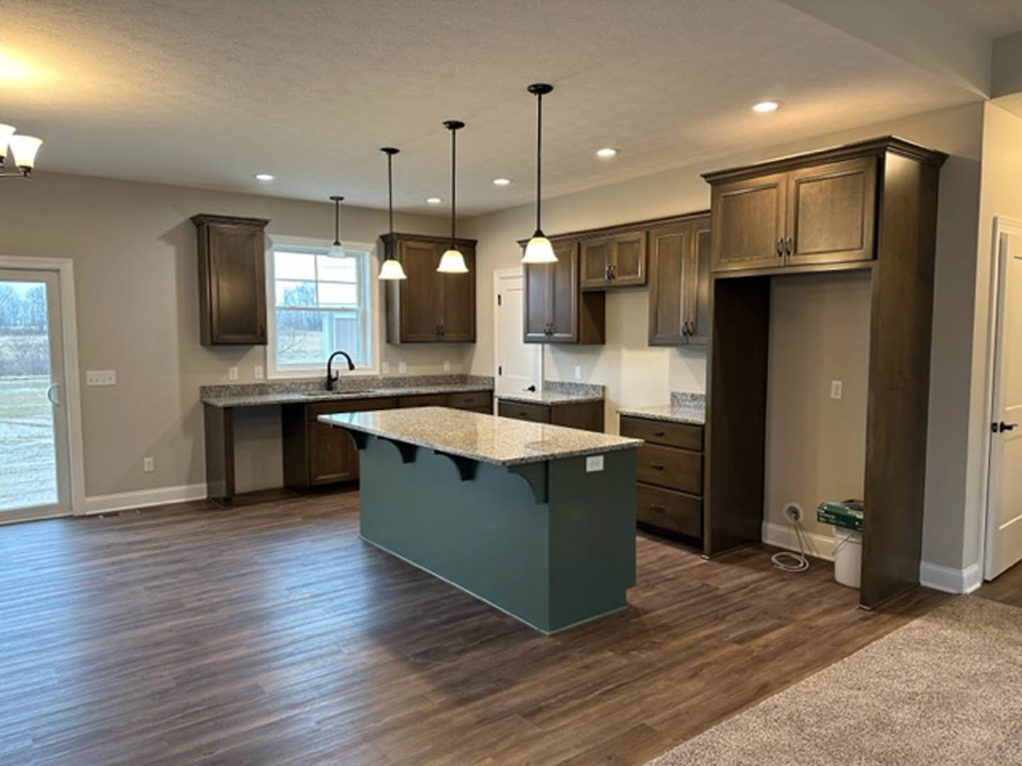 Modern kitchen featuring a central island with marble countertop, white cabinetry, stainless steel sink, tile flooring, and a window with a black handle.