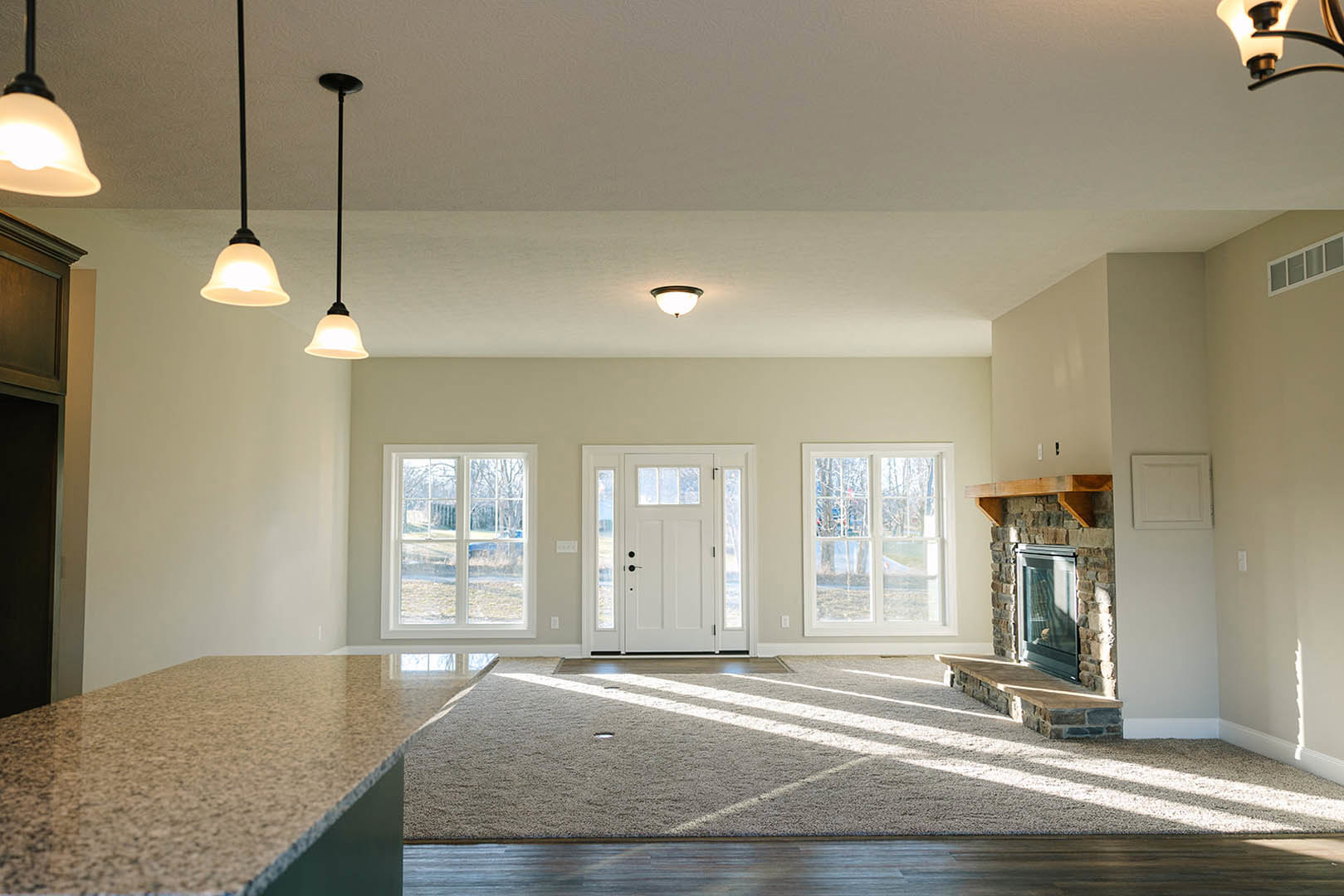 Living room featuring a stone fireplace, tile flooring, round ceiling light fixture, white door with glass panels, and large window overlooking the yard