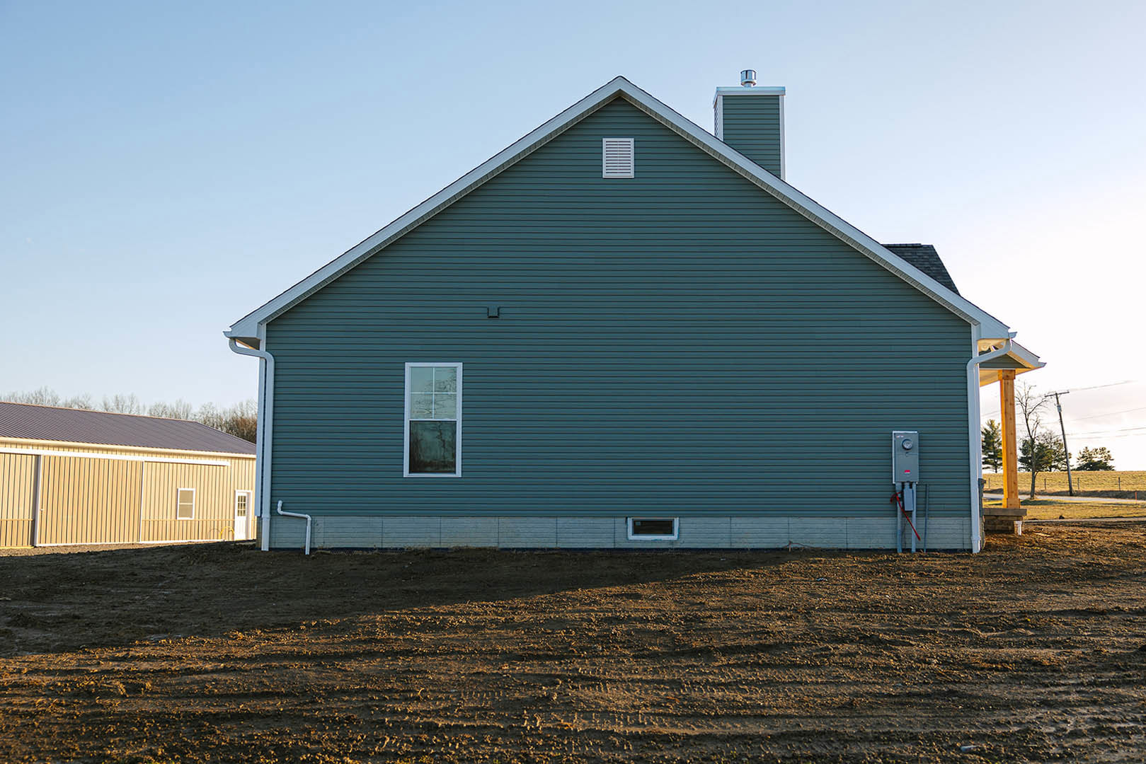 Blue siding house with expansive metal roof, white framed window, and white vent on side wall against clear sky