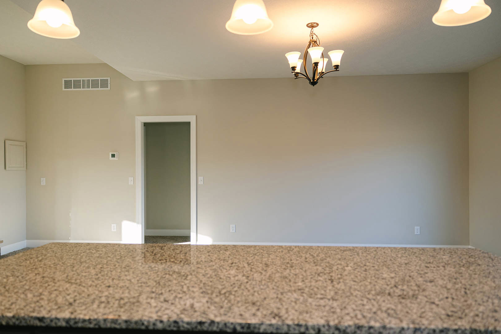 Marble kitchen countertop with white cabinetry, black hardware on a nearby door, modern chandelier and ceiling light fixtures, plaster walls, and light wood flooring