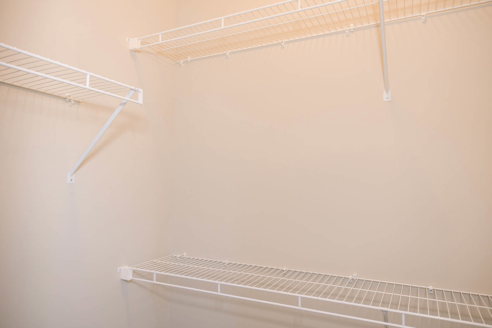 White metal wire shelf mounted on a plaster wall in a room with white finishes.