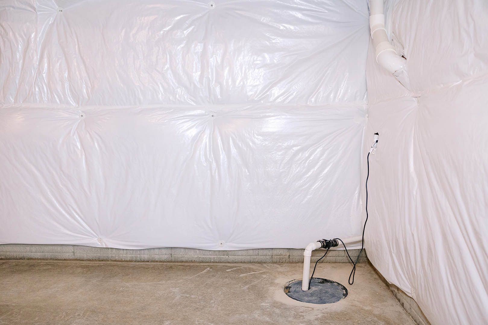 White plastic sheeting covering concrete floor with exposed white pipe, black wire, and hole in ground