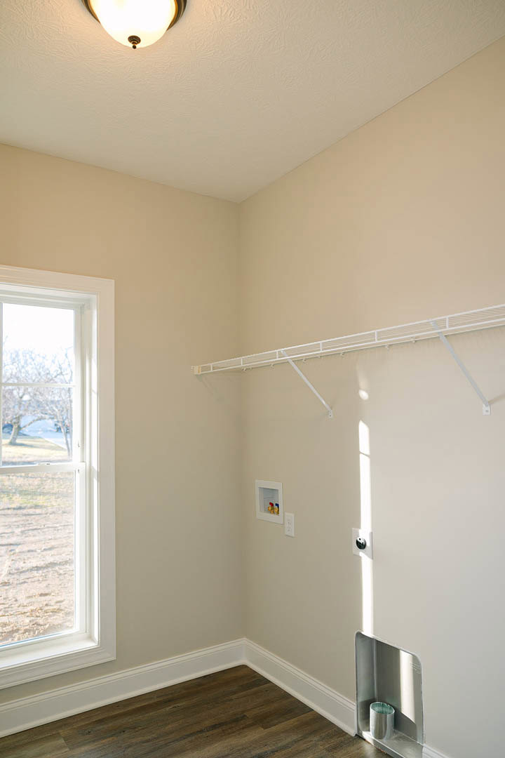Walk-in closet with white shelving, white door, wood flooring, and white metal railing above a white wall; window offers view of tree outside, ceiling fan and light fixture visible