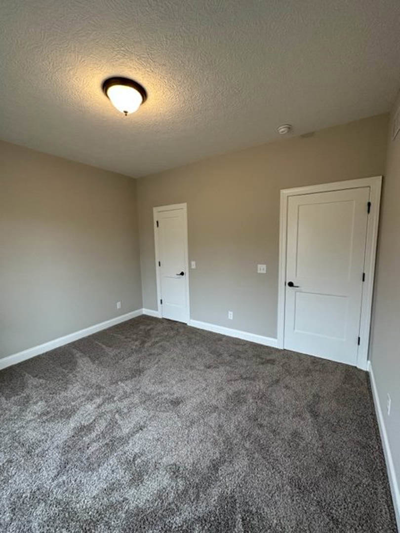 Carpeted room with two white doors featuring black handles, light fixture on white ceiling, pale walls, and close-up view of textured carpet
