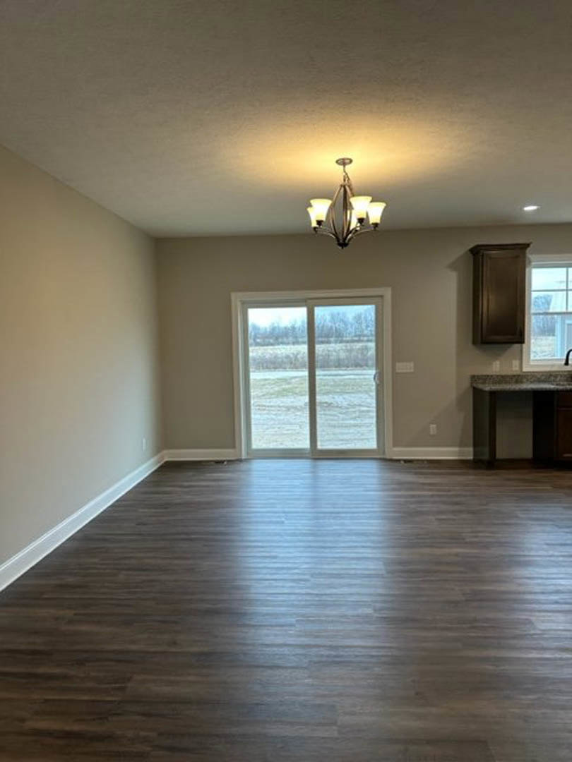 Wood-floored room featuring a sliding glass door opening to a grassy field, white walls, a marble-topped table, and a five-light ceiling fixture.
