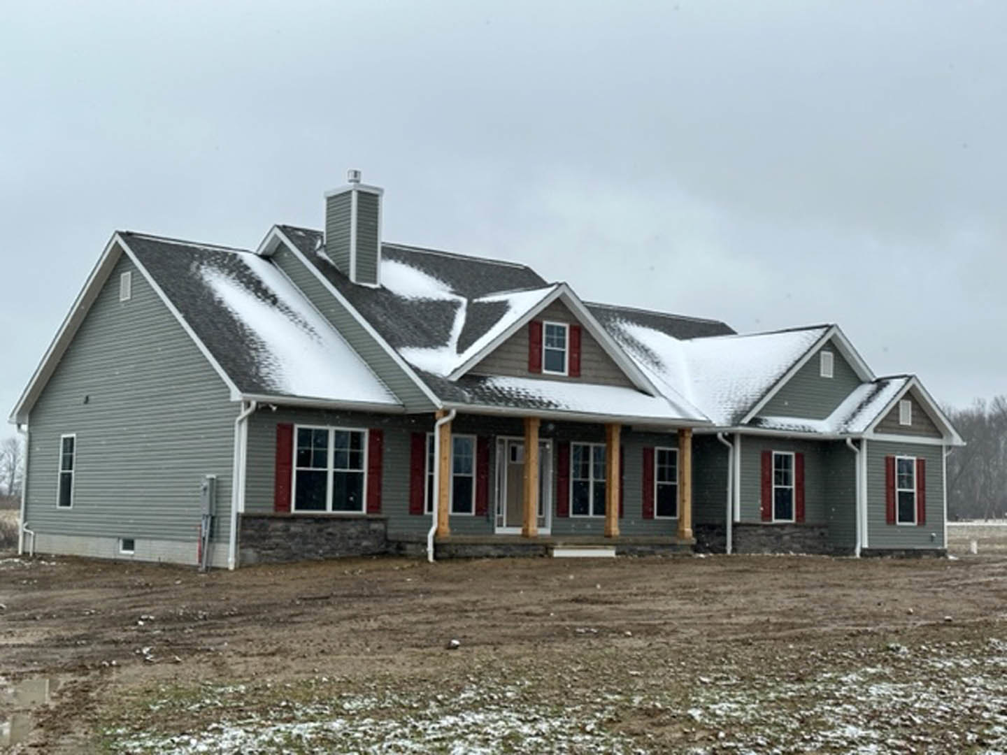 Two-story house with white-framed windows, light-colored siding, and snow covering the roof and ground, set against a cloudy sky