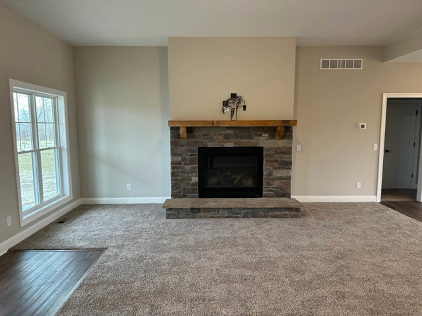 Living room with beige carpet, wood-burning fireplace with black frame and glass window, white door with black knobs, window overlooking grassy yard, close-up of wood flooring