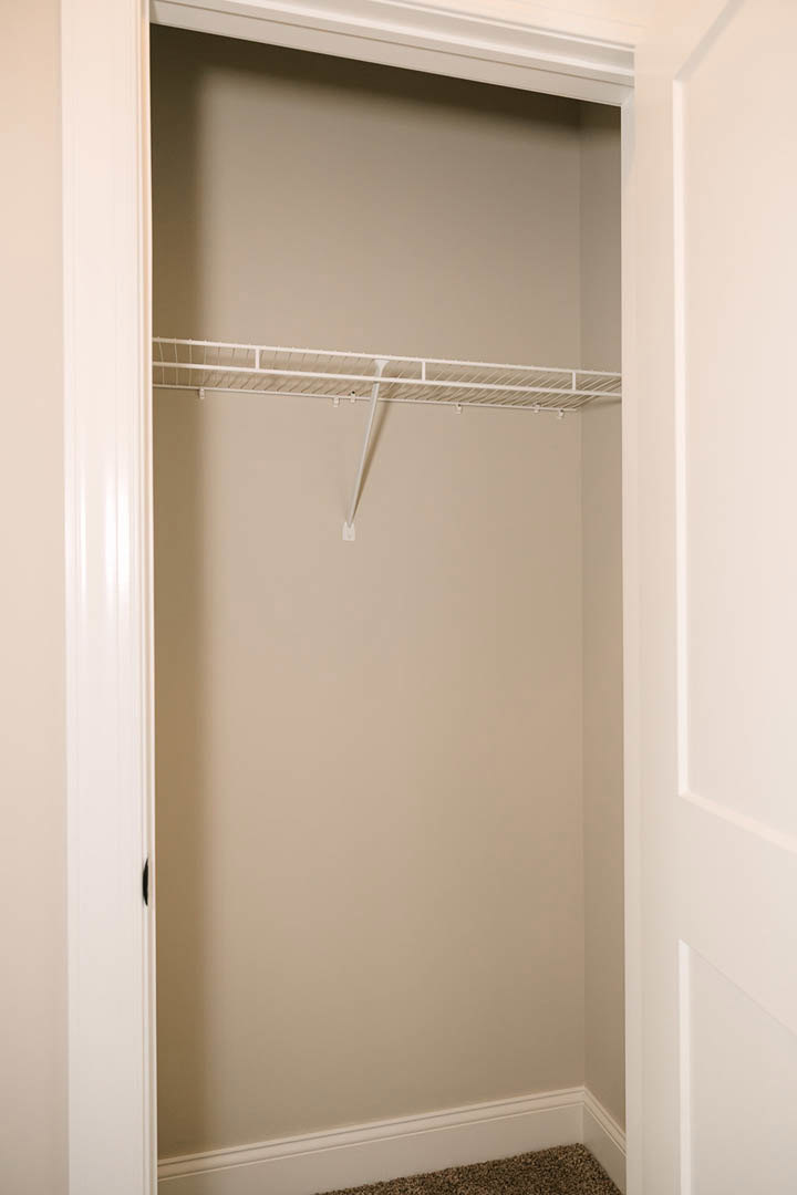 White closet interior featuring a white shelf with a long metal rod, white walls, and baseboard trim.