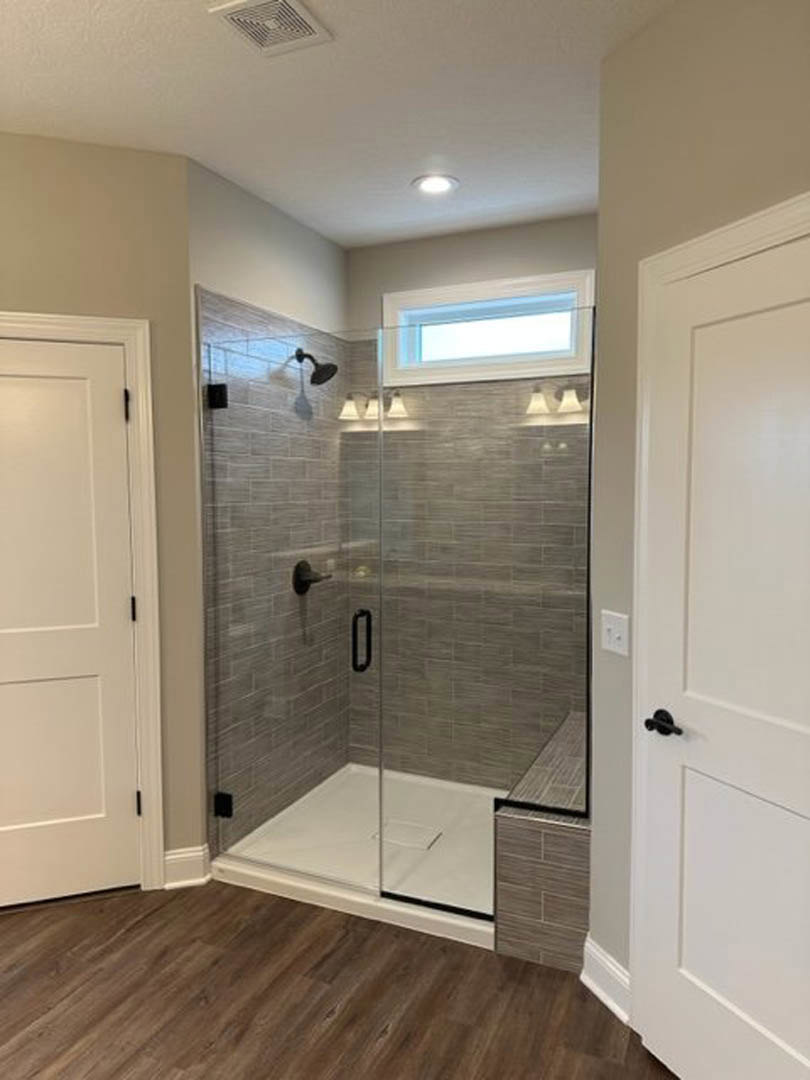 Bathroom featuring a frameless glass shower enclosure, wood plank flooring, and white tile walls
