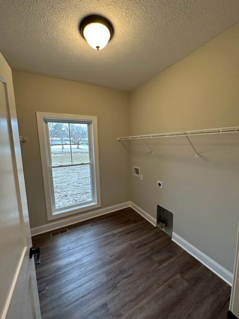 Sunlit room featuring wide plank wood flooring, large window overlooking snowy field, white plaster walls, ceiling-mounted light fixture, and white wire mesh panel on one wall.