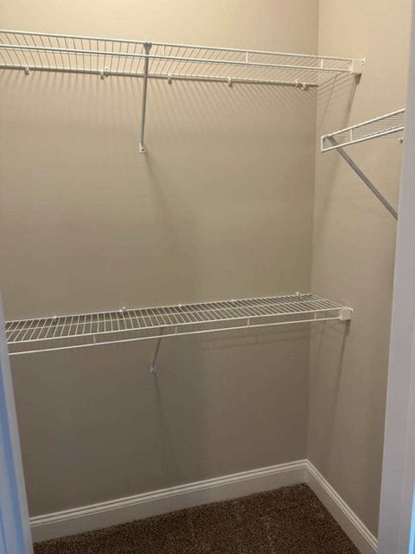 Walk-in closet with white metal shelving, carpeted floor, and a closed white door against smooth painted walls