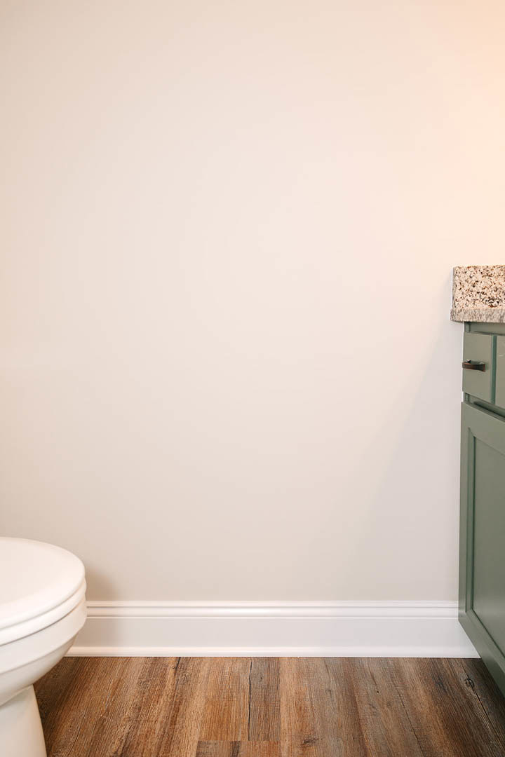 Modern bathroom featuring a white toilet, rectangular sink with chrome faucet, light tile flooring, and white plaster walls with a green-framed accent.