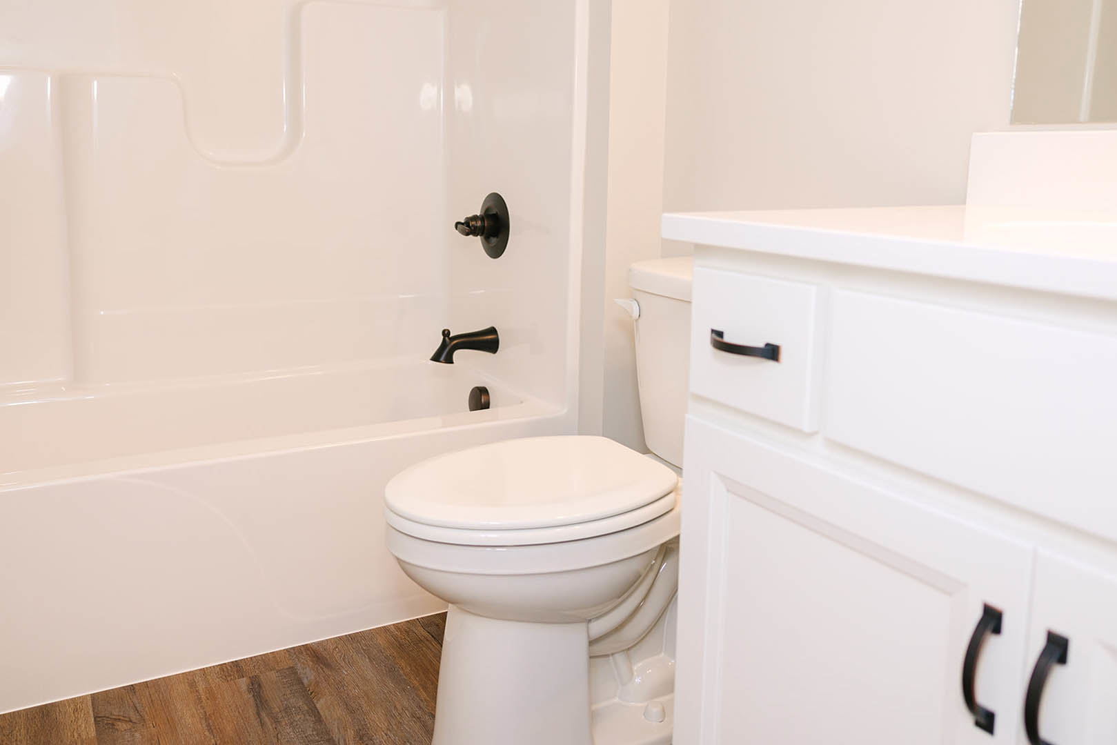 White bathtub and toilet with closed seat, chrome faucet, light tile walls, and bathroom accessories.