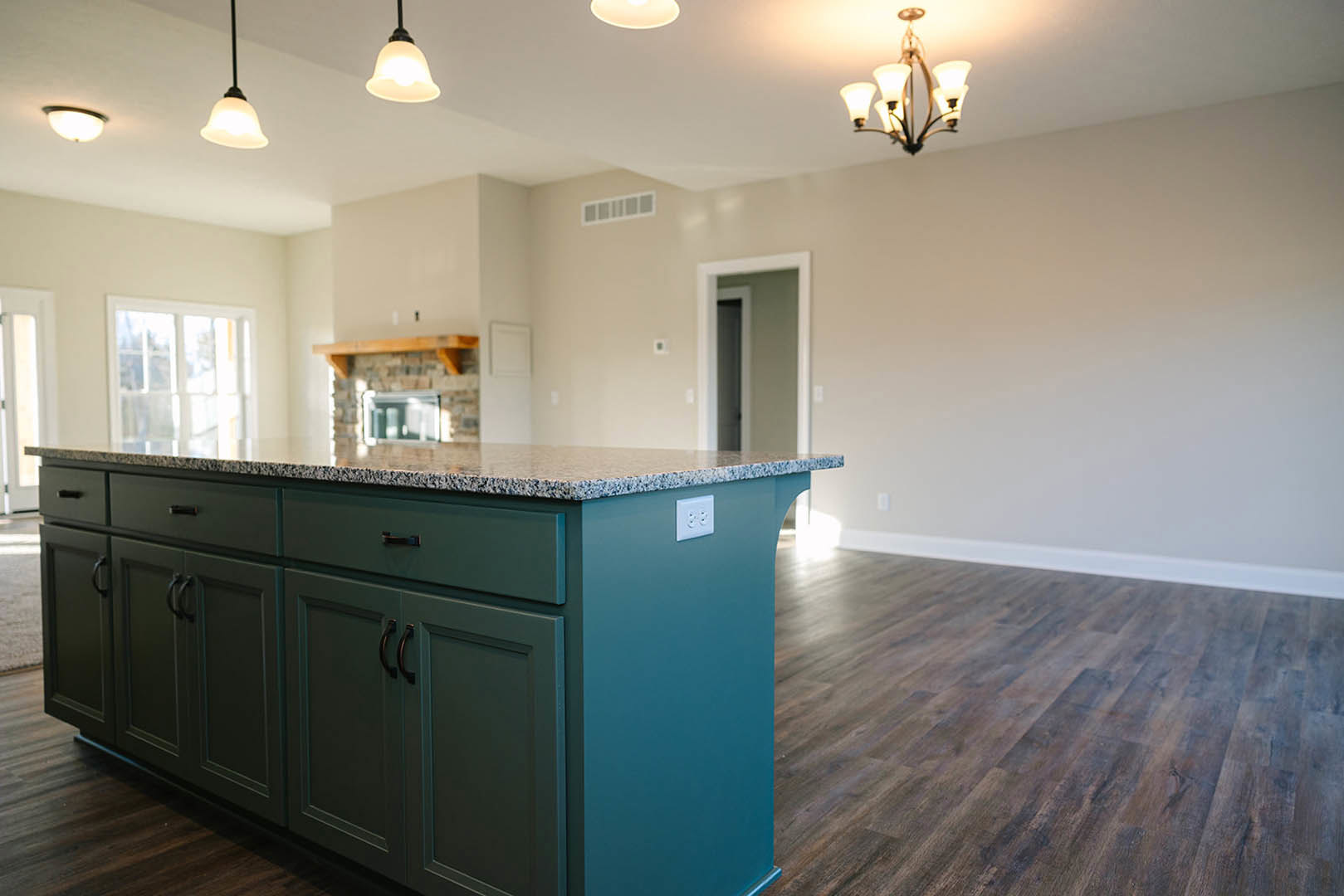 Marble-topped kitchen island with built-in sink, white cabinetry, wood flooring, and modern light fixture overhead