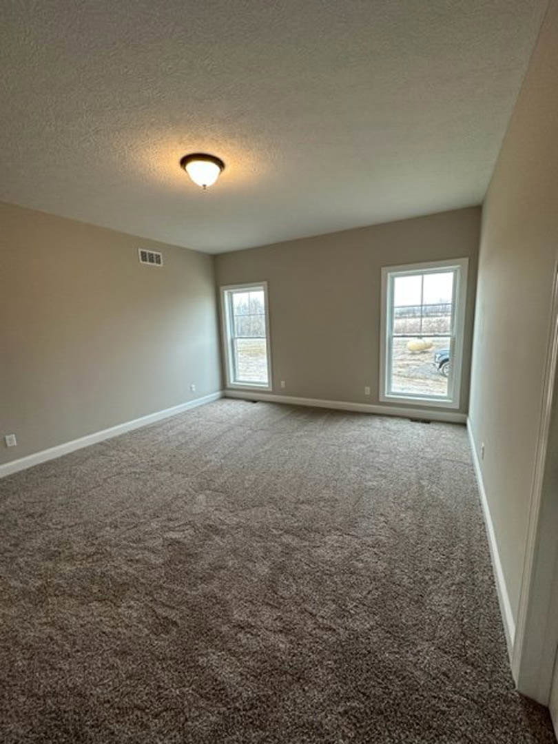Brown carpeted room with white-framed windows, ceiling light fixture, and parked car visible outside