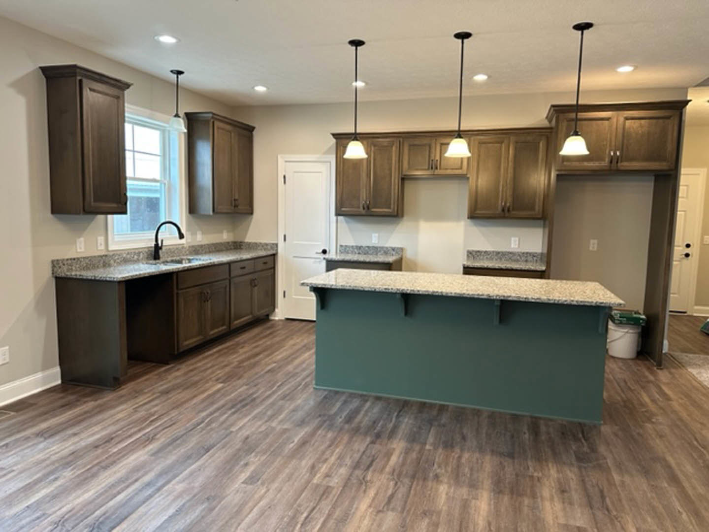 Granite countertops, white cabinets, stainless steel faucet, tile backsplash, white door with black handle, white bucket with green handle on floor