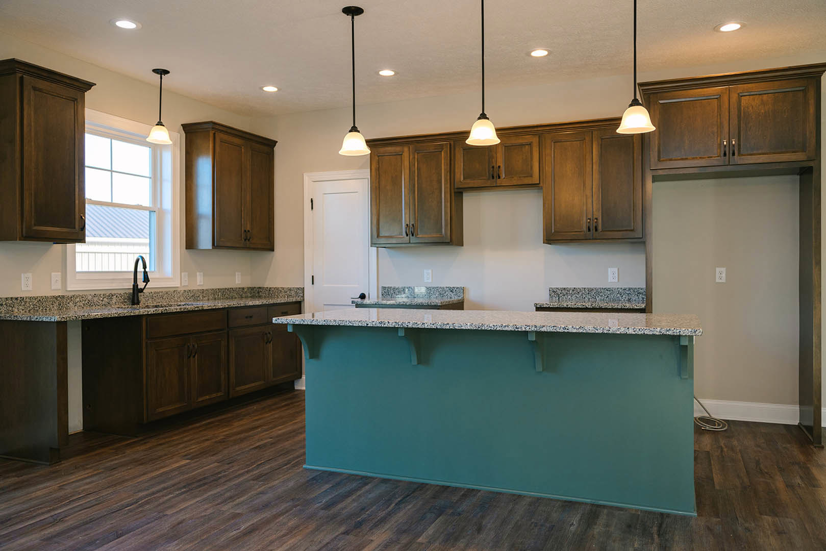 Kitchen with granite countertops, wood flooring, white-framed window, dark metal support poles, and close-up of cabinetry