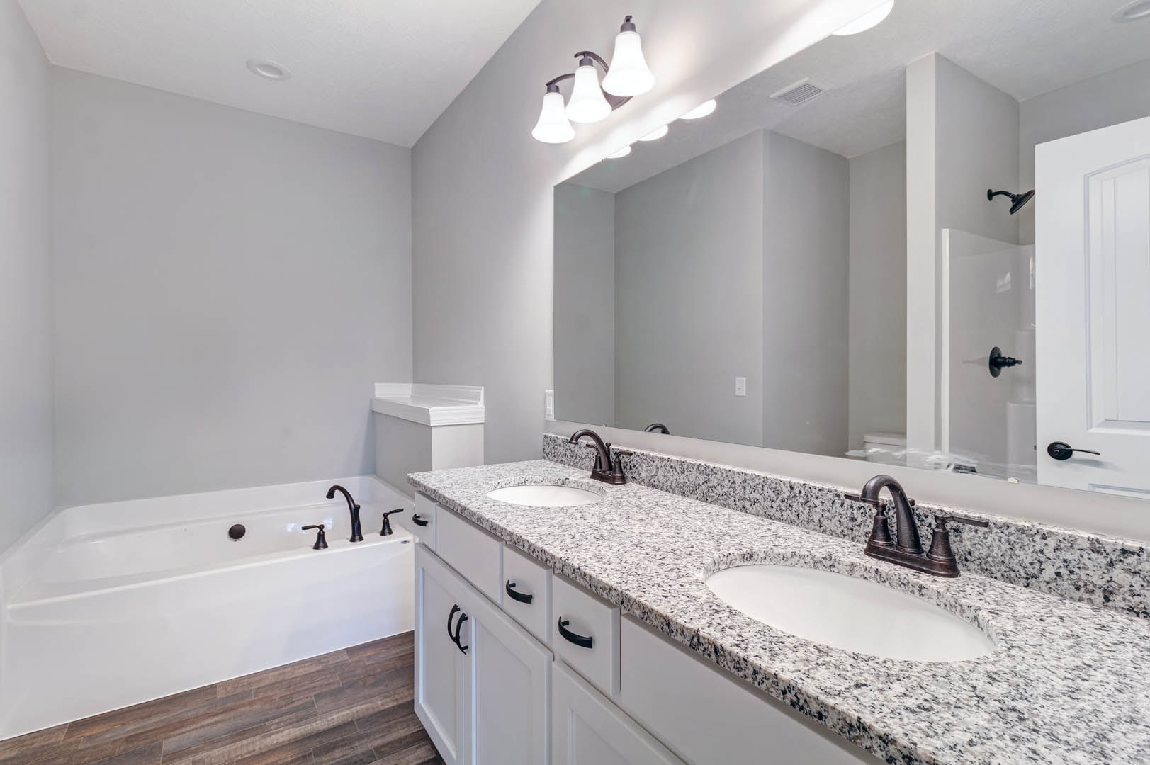 Marble countertop with white sink and chrome faucet, freestanding bathtub, wood flooring, and modern light fixture in a bathroom