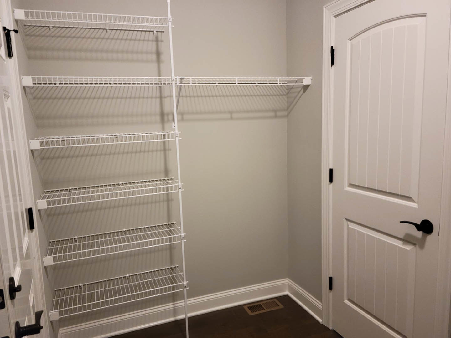 White built-in shelves against a paneled wall in a room, with a nearby door, visible pipe with black handle, and vent on the surface.