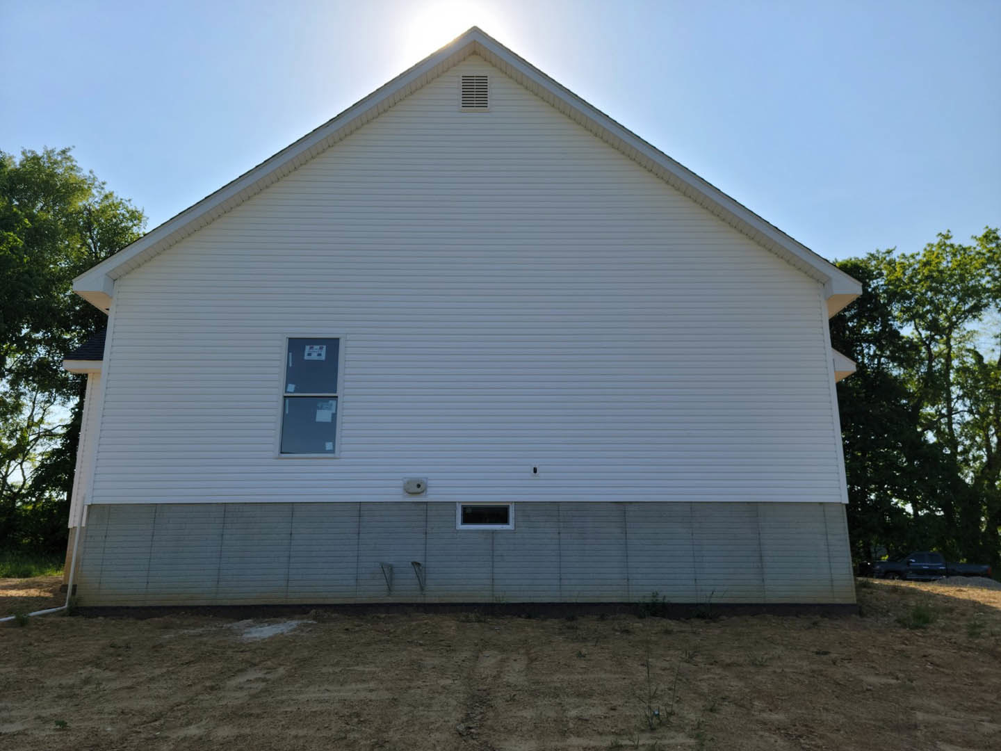 White siding house with single window displaying papers, wall vent, and dirt yard bordered by metal fencing.