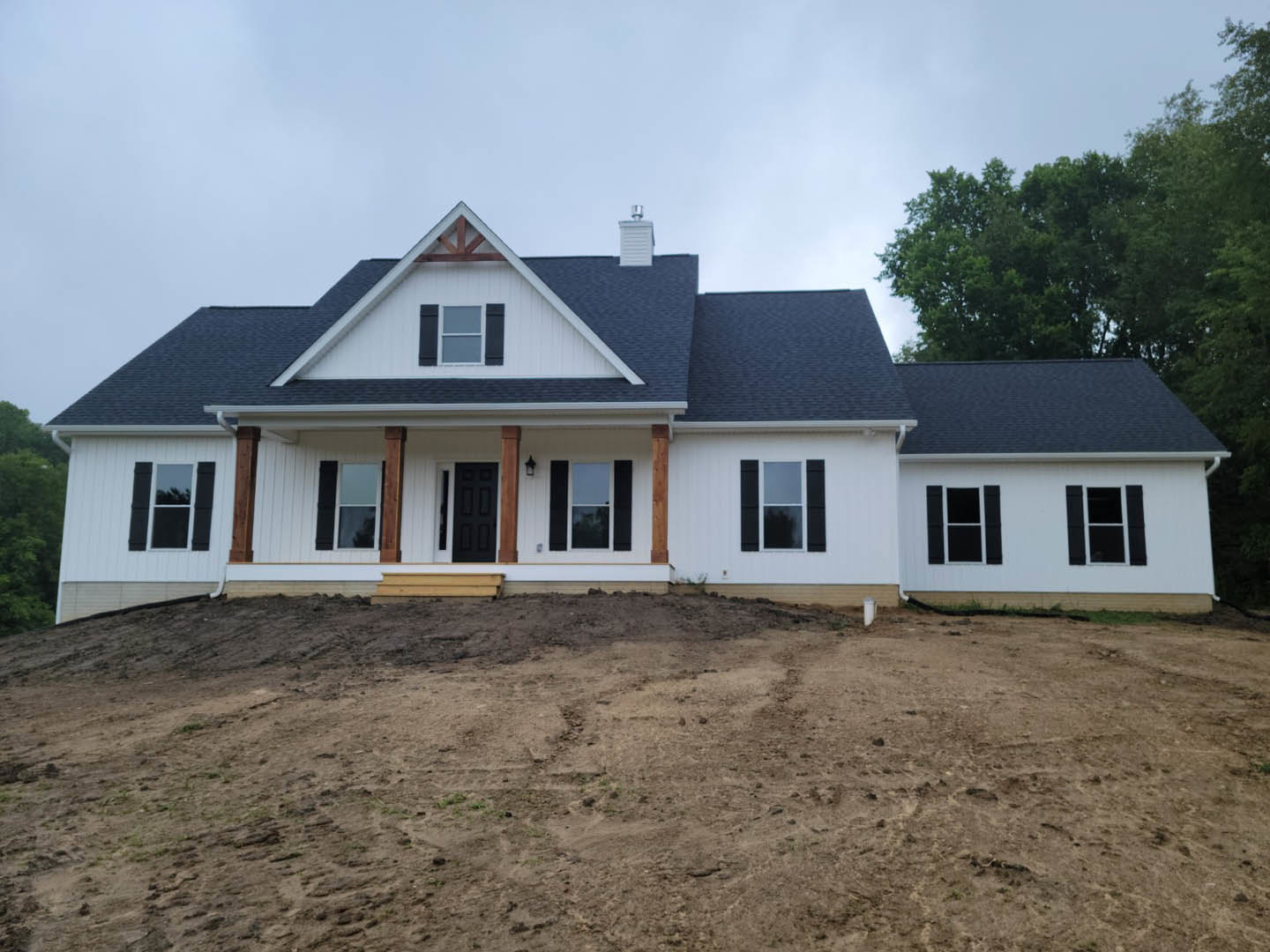 White modern house with black door and window frames, chimney, and flat roof, set against a dirt hill and open field under a clear sky.