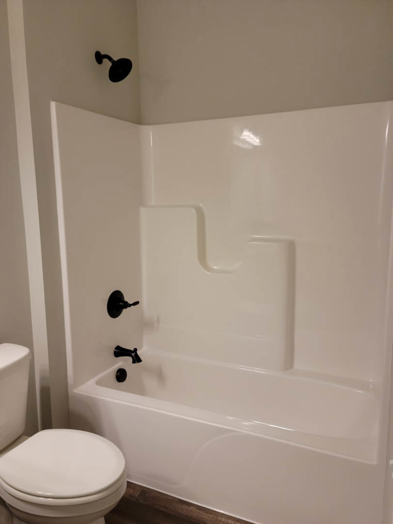 White freestanding bathtub and matching toilet on light tile floor, black shower head mounted on white tiled wall