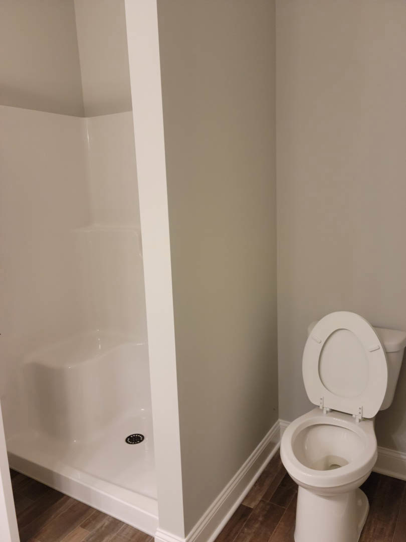 White tile bathroom with open toilet seat, glass shower enclosure, and chrome fixtures