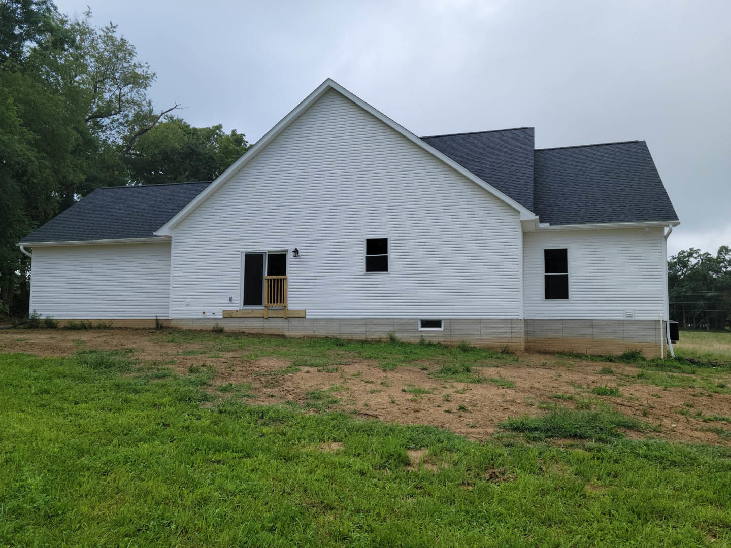 White farmhouse with white-framed windows, wooden porch, black vent, and grassy lawn under a partly cloudy sky.