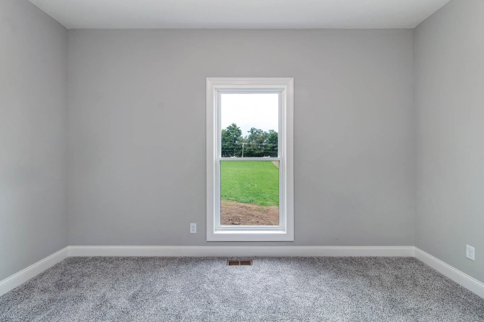 Bright room with white plaster walls, large window overlooking green lawn and distant trees, light wood flooring, ceiling vent visible