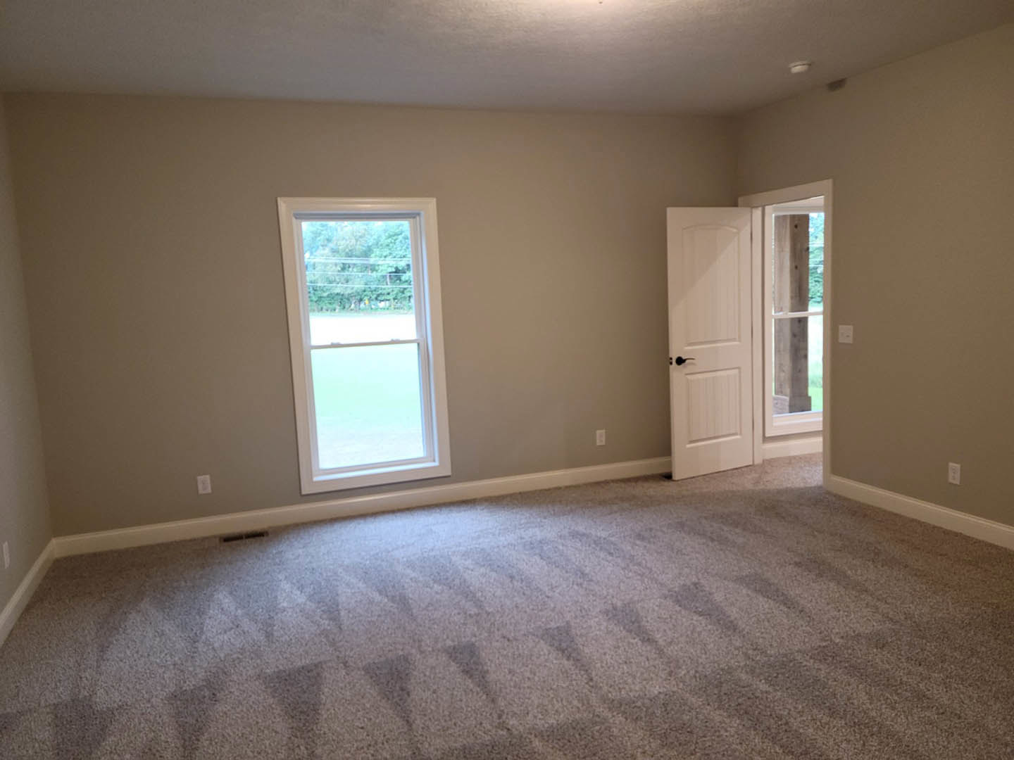 Carpeted room with geometric pattern, white door, two white-framed windows, neutral walls, and plaster ceiling.