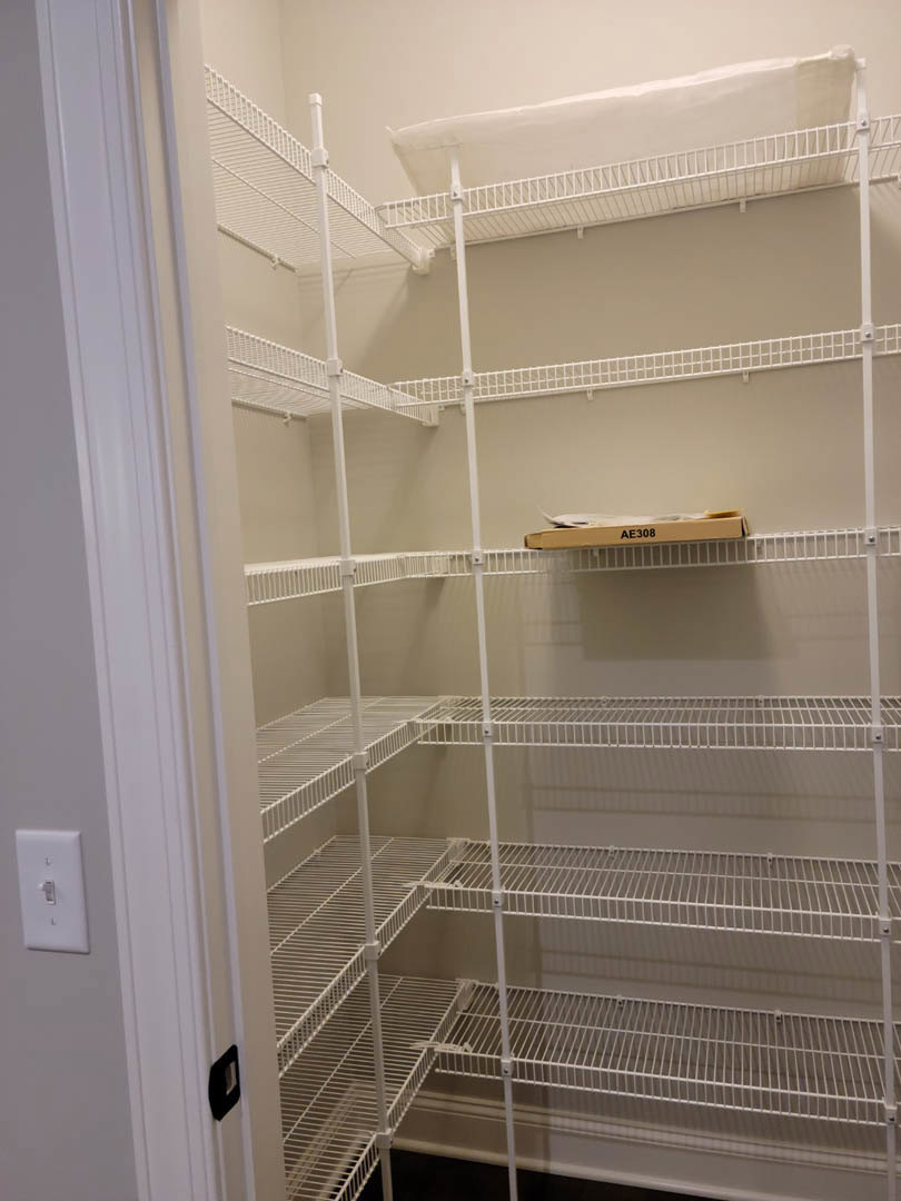White wire shelves installed in an empty closet, with a cardboard box placed on one shelf and a light switch visible on the adjacent wall.