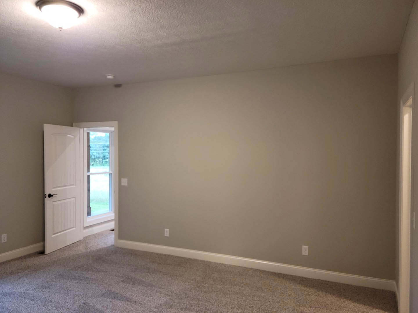 Carpeted room with white baseboards, two white doors, window with white frame, and ceiling-mounted light fixture
