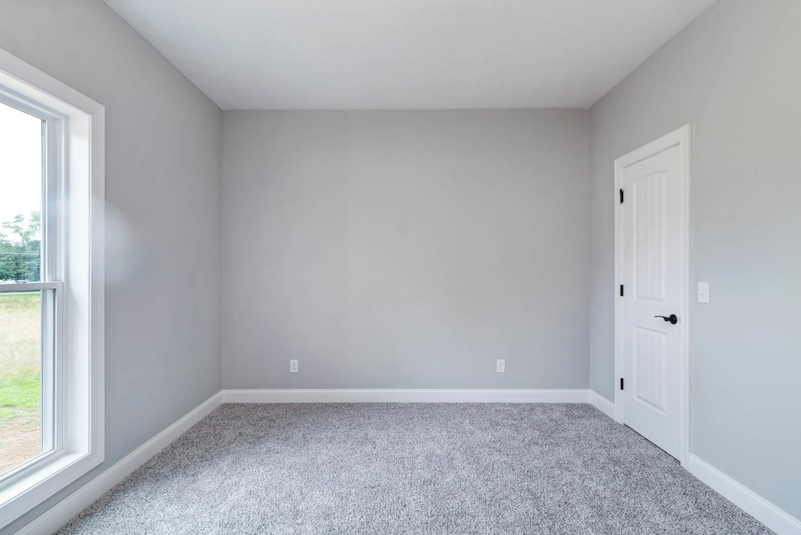 Carpeted room with white walls, white door, window showing cloudy sky, and visible electrical outlets